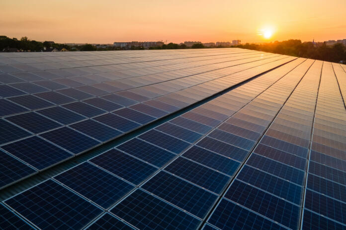 Blue photovoltaic solar panels mounted on building roof for producing clean ecological electricity at sunset. Production of renewable energy concept.