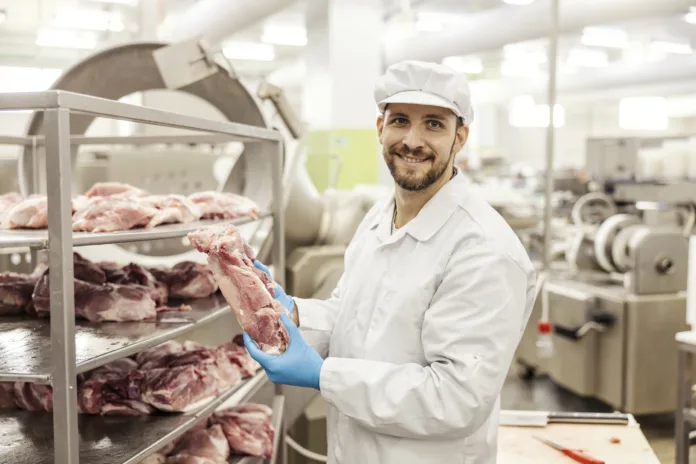 A meat industry laborer is holding a piece of fresh raw meat and smiling at the camera.