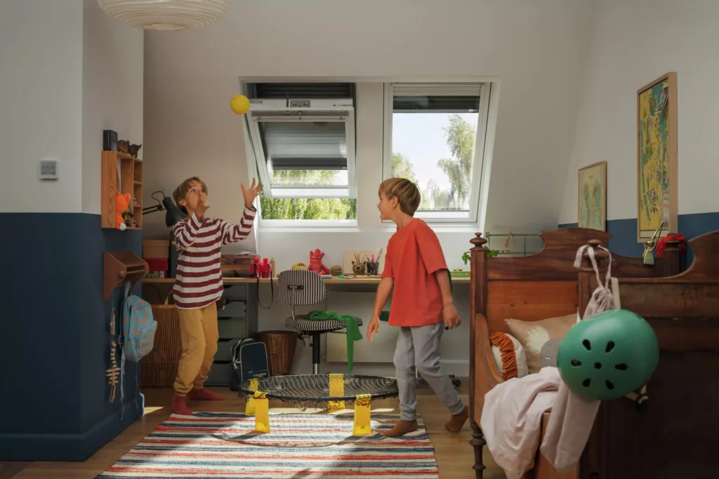 Otroka se igrata v podstrešni sobi, opremljeni s strešnimi okni Vellux