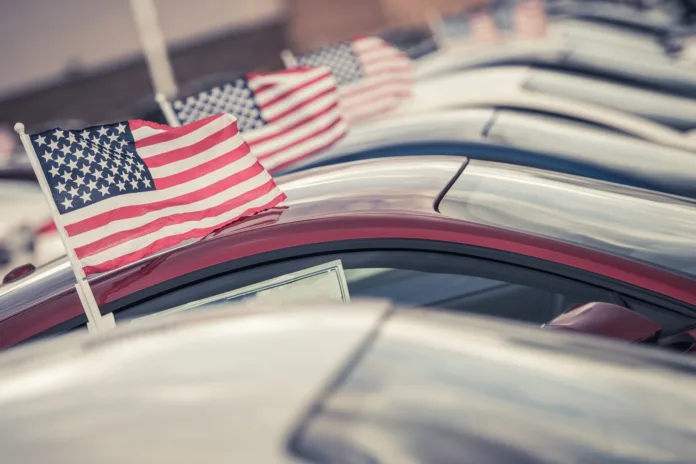 American Made Cars Sale Concept Photo. United States Economy and Market Theme. Brand New Vehicles For Sale with American Flags Attached. Dealership Lot.