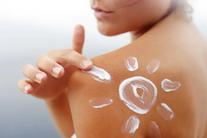 Dark tanned body of young woman in summer with sunscreen  lotion in shape of sun