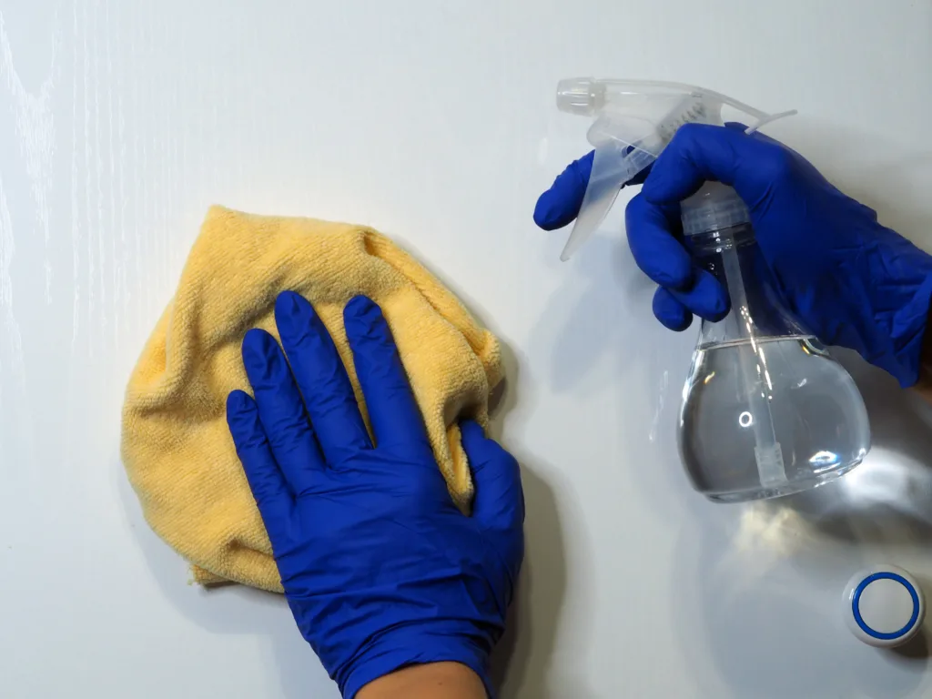 Close-up of a female's hands in bleu protective rubber gloves cleaning kitchen cabinets with white vinegar. Cleaning the kitchen from dirt, grease and dust without household chemicals.