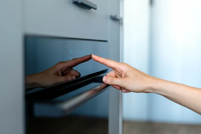 Cropped view on woman hand press sensor button of modern electric oven to cooking dinner. Female finger choose program on touch control panel with indicators. Household baking appliances at kitchen