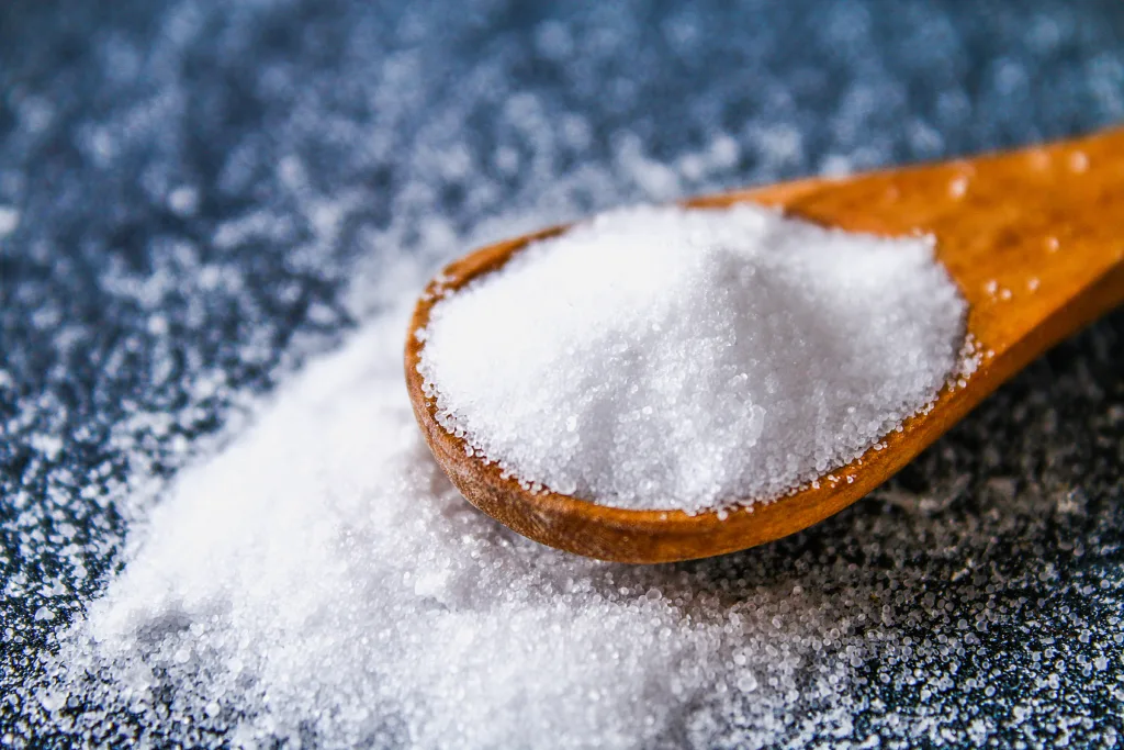 Crystals of shallow salt in a scoop, spoon on a dark gray table. Background for advertising salt. Table salty. Salted food