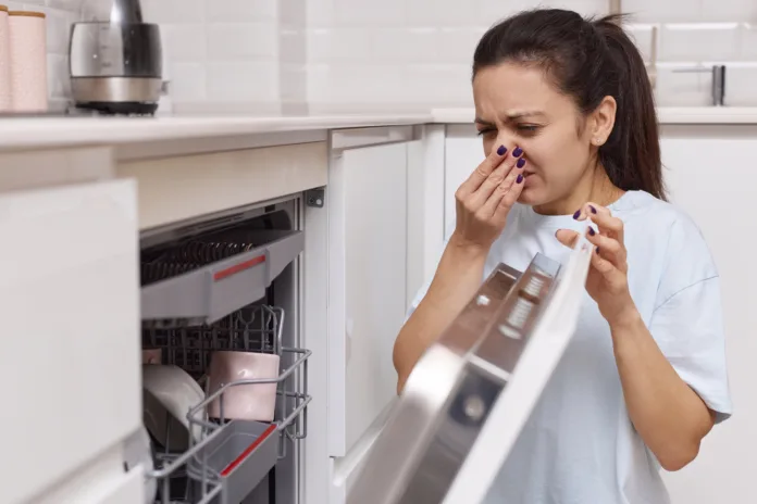 woman smells strange and terrible smell coming from dishwasher machine in kitchen