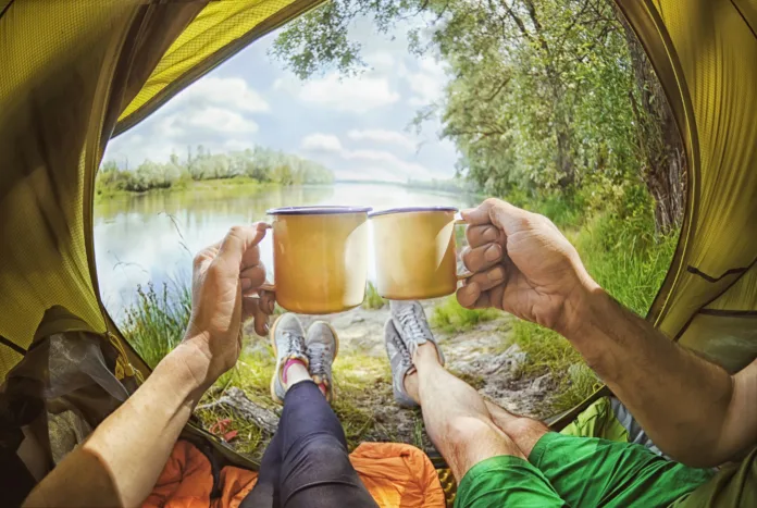 Young couple sitting   in the tent and drinking tea while looking on the Desna river , Ukraine