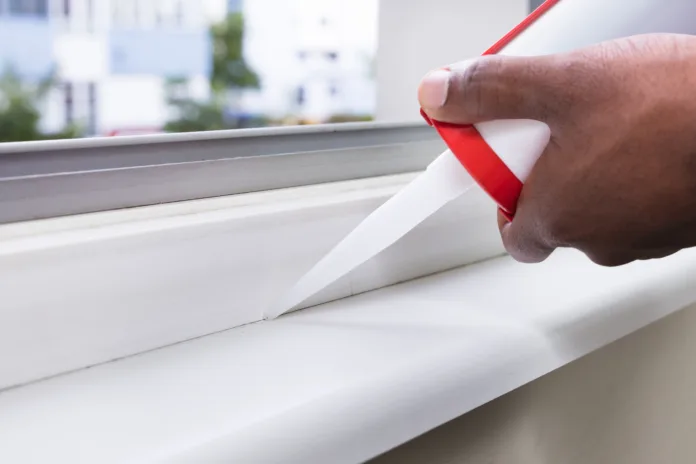 Close-up Of Person Hand Applying Silicone Sealant With Silicone Gun On Window