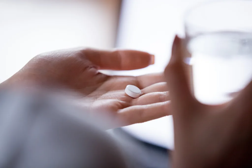 Close up woman holding pill in hand with water. Female going to take tablet from headache, painkiller, medication drinking clear water from glass. Healthcare, medicine, treatment, therapy concept