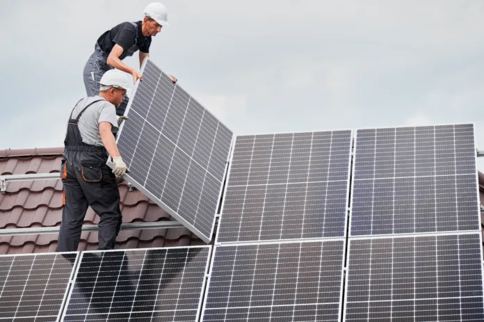 Men technicians mounting photovoltaic solar moduls on roof of house. Builders in helmets installing solar panel system outdoors. Concept of alternative and renewable energy.