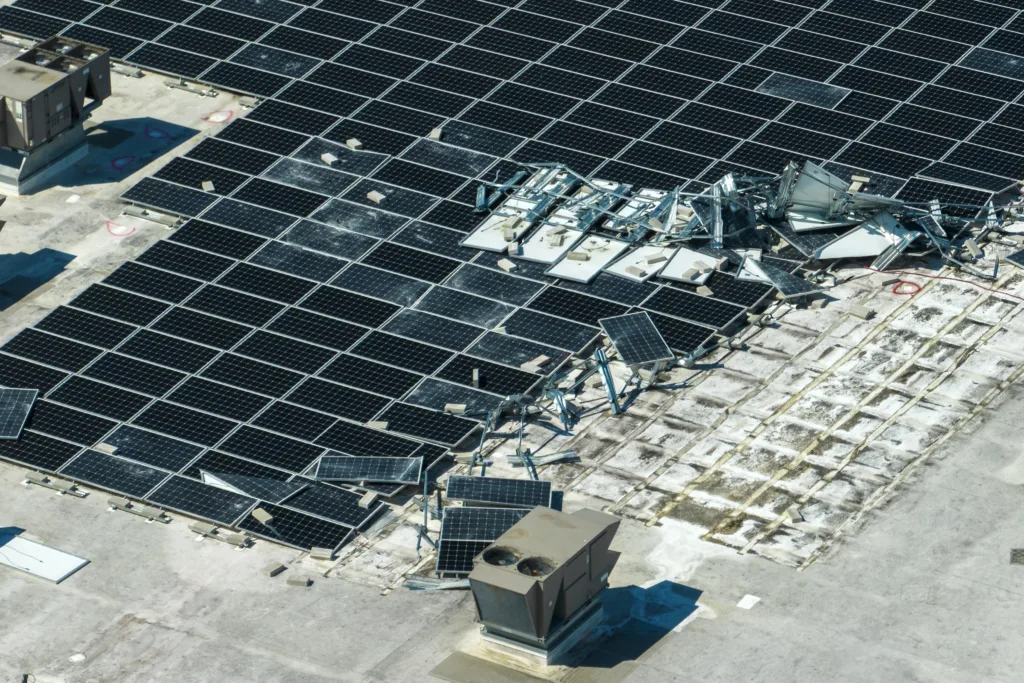 Photovoltaic solar panels destroyed by hurricane strong wind mounted on industrial building roof for producing green ecological electricity. Consequences of natural disaster in Florida.