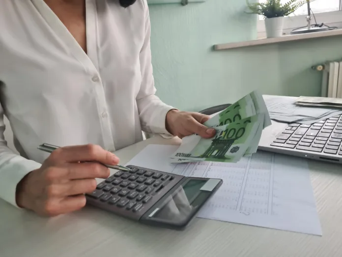 Woman is counting on calculator and writing with pen in notebook closeup. Financial budget and payment of taxes