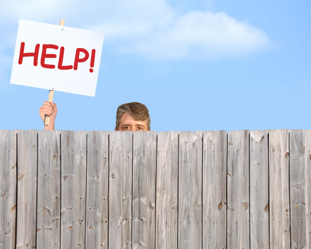 A man holding a HELP sign is peering over a fence desperate for help with his many problems in addiction, bipolar disorder, depression or could represent a man in need of anything imaginable.