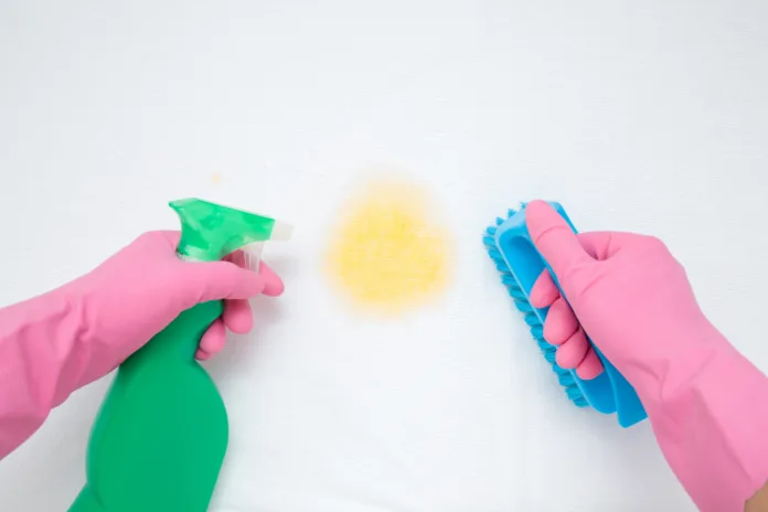 Hands in rubber protective gloves holding spray bottle and brush. White mattress cleaning. Urine stain from baby, kid, children, adult people or pet. Point of view shot. Close up. Top view.