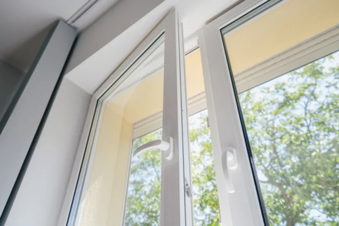 low angle view of plastic pvc window with white metal frame installed at modern house, blurred green trees outside the room