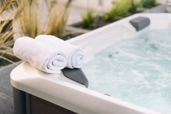 Selective shot of white dry towel folded on edge of hot tub in natural sunlight on residential backyard garden. Bath on terrace. Bathtub with bubble water on hotel roof at sunset light