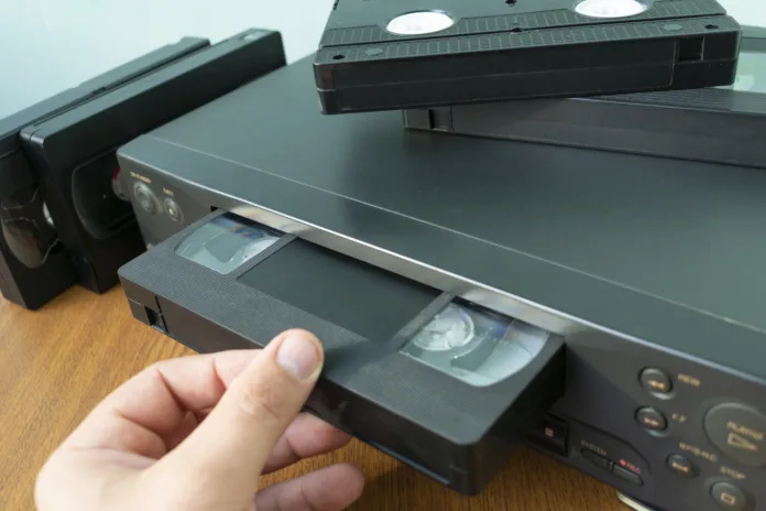 VHS videocassette is put into the video recorder to watch the video, another video cassette is on the video-tape recorder