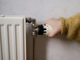 Hand turning off the heating, radiator while wearing a warm yellow sweater. Concept of saving electricity and heating as a way of energy saving consumption.