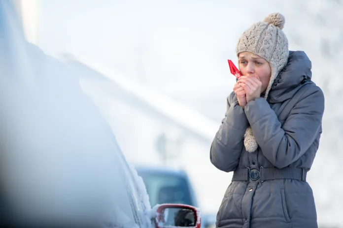 Young woman cleaning her car from snow and frost on a winter morning, she is freezing and needs to get to work