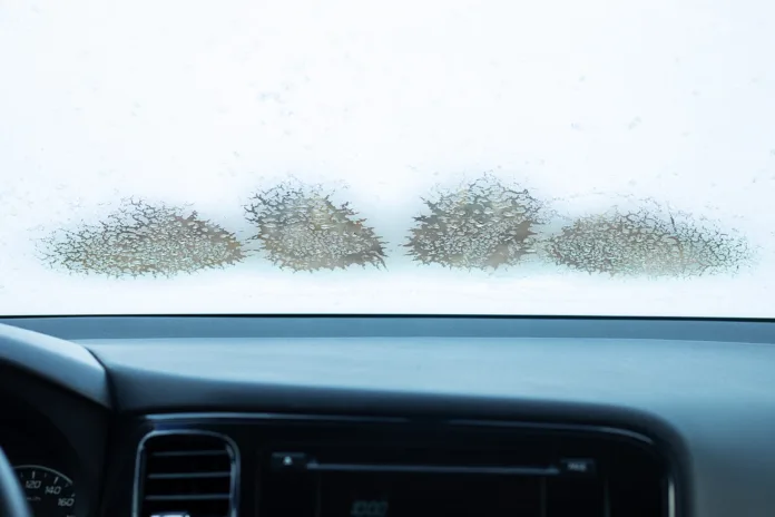 frozen car windshield in winter, inside the car, cold temperature, melting ice on the window, working climate control. Close-up photo with copy space