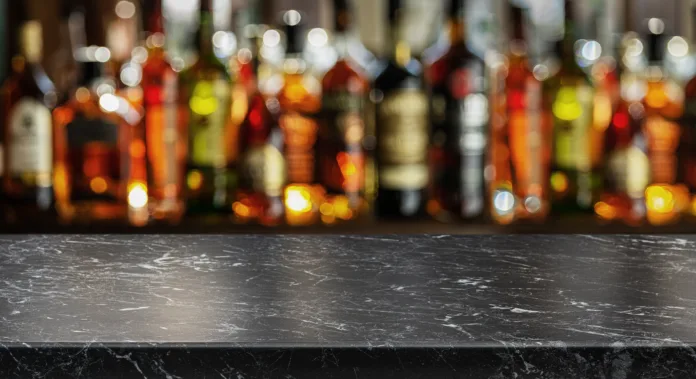 Grey table top and beautiful bokeh shelves with alcohol bottles at the background. Bar concept.