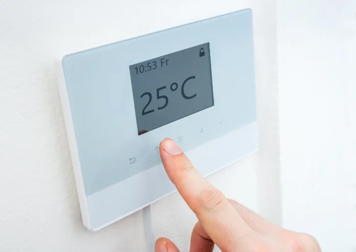 Heating concept. Hand is adjusting temperature in room on digital central thermostat control.