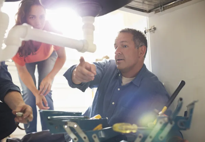 Plumbers working on pipes under sink